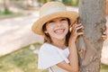 Laughing little girl with lightly-tanned skin posing in park touching tree. Outdoor close-up portrait of cheerful dark Royalty Free Stock Photo