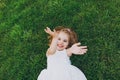 Laughing little pretty child baby girl in light dress lie on green grass lawn, waving hands in park. Mother, little kid Royalty Free Stock Photo