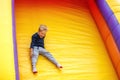 Laughing, lot of fun little boy child sliding on an inflatable multi-colored slide. Bright yellow background, free space for text