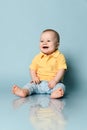 Laughing loud infant baby child boy toddler in blue jeans and yellow polo shirt is sitting on the floor