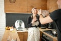 Laughing lovely family of woman in apron and rearview man holding flour bowl and fooling around against kitchen drawers