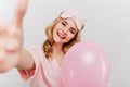 Laughing lovely girl in sleepmask making selfie in her birthday. Photo of blissful curly woman with pink balloons