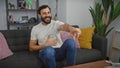 Laughing man with beard sitting on sofa in modern living room pointing at camera Royalty Free Stock Photo
