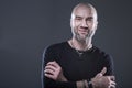 Laughing man. A brutal bald unshaven guy in a black shirt crossed his arms. Confidence and positivity. Dark gray background Royalty Free Stock Photo