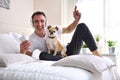 Laughing man listening music lying in bed with chihuahua