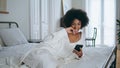 Laughing model watching phone funny video home. Relaxed african lady laying bed