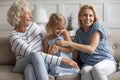 Laughing mommy and granny tickling with little girl on couch