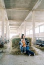 Laughing mother with a little girl on her knees sits on a haystack and looks at the eating goats in the paddocks Royalty Free Stock Photo