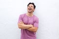 Laughing older man standing with arms crossed against white wall and looking up