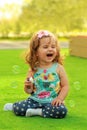 Laughing one year old girl learning to blow soap bubbles and sitting on the sunlit lawn
