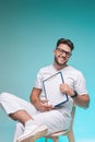 Laughing optimistic male physician practitioner in glasses hold blank space sheet. Studio portrait on blue background Royalty Free Stock Photo