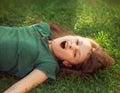 Laughing playful crazy crying kid girl lying on the grass on nature summer background. Closeup Royalty Free Stock Photo