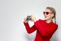 Laughing and Positive Caucasian Blond Girl With Old School Film Camera in Red Dress with Sunglasses. Taking Pictures Against White Royalty Free Stock Photo