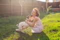 Laughing positive young woman in dress plays with her beloved restless dog sitting in the yard of a country house on a