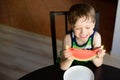 Laughing preschooler eats a watermelon at the table