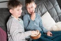 Laughing school aged boys sit on sofa, eat popcorn and watch comic TV show. Kids having fun and relaxing at home. Royalty Free Stock Photo