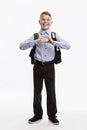 Laughing schoolboy in uniform with a backpack shows his heart with his hands. Back to school. White background. Vertical