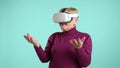 Laughing senior lady standing over blue background, thrilled by using VR headset