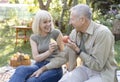 Laughing senior spouses sitting on field grass and eating fruits, talking and smiling, resting outdoors in their garden Royalty Free Stock Photo