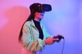 Laughing smiling surprise girl in neon with VR glasses holds a gamepad in her hands and plays games. Virtual world, technology Royalty Free Stock Photo