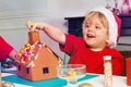 Laughing toddler decorate gingerbread house, finger near chimney