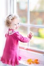 Laughing toddler girl watching out of the window in autumn