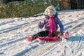 Laughing, vibrantly dressed young girl with blue ear muffs sledging down a slope Royalty Free Stock Photo