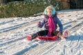 Laughing, vibrantly dressed young girl with blue ear muffs sledging down a slope