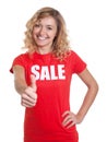 Laughing woman with blond hair in a sale shirt showing thumb