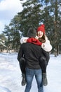 Laughing woman keeps hands in heart shape sign sitting on her guy hands. Young loving couple in winter forest