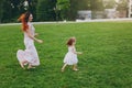 Laughing woman in light dress running catching up with little cute child baby girl on green grass lawn in park. Mother Royalty Free Stock Photo