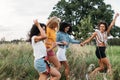 Laughing woman runs in front of her friends with a raised hand. Group of four young females on summer vacation