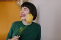 Laughing woman with short straight hair holding yellow tulip. Studio portrait of pleasant white girl in green attire Royalty Free Stock Photo