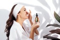 Laughing woman in a white bathrobe takes care of her skin and moisturizes it her face with a serum