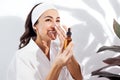Laughing woman in a white bathrobe takes care of her skin and moisturizes it her face with a serum