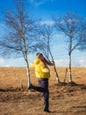 Laughing woman in a yellow jacket jumps on an autumn field against a blue sky on a sunny day. Royalty Free Stock Photo