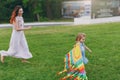 Laughing woman in light dress and little cute child baby girl running, catching up and play with colorful kite in park Royalty Free Stock Photo