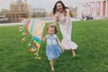 Laughing woman in light dress and little cute child baby girl running, catching up and play with colorful kite in park Royalty Free Stock Photo