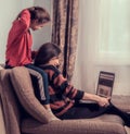 Laughing woman working at home on computer and cute kid play with mother. Sitting on sofa, daughter covering mother the eyes with Royalty Free Stock Photo