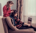 Laughing woman working at home on computer and cute kid play with mother. Sitting on sofa, daughter covering mother the eyes with Royalty Free Stock Photo