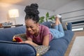 Laughing young adult woman lying on sofa with smartphone