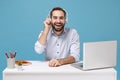 Laughing young bearded man in light shirt sit work at desk with pc laptop isolated on pastel blue background