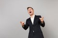 Laughing young business man in classic black suit and shirt mocking, pointing index fingers on camera isolated on grey Royalty Free Stock Photo
