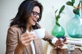 Laughing young businesswoman texting with her mobile phone in the coffee shop.