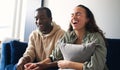 Laughing Young Couple Relaxing At Home Sitting On Sofa Whilst Watching Comedy Show On TV Together