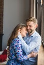 Laughing young couple stands at the window and gently hugs