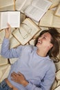 A laughing young girl in a blue sweater and jeans lies on a pile of open books reading. Education and knowledge. Vertical Royalty Free Stock Photo