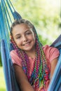 Laughing young girl with colorful braids is posing on hammock