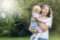 Laughing young woman with her little daughter in her arms in the park on a sunny summer day. Mom in a white T-shirt and jeans hugs Royalty Free Stock Photo