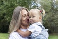 Laughing young woman with her little daughter in her arms in the park on a sunny summer day. Mom in a white T-shirt and jeans hugs Royalty Free Stock Photo